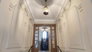 A grand hallway with ornate wall moldings, a chandelier, and a wooden door at the end. - Exceptional Penthouse, 2 BDR Suites, 3 spacious terraces, Sea view, Elevator, AC (Nice)
