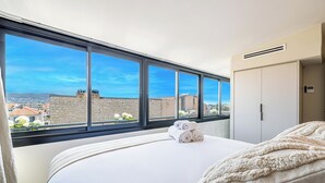 A hotel room with a large window, a bed with white linens, and a view of the cityscape. - Exceptional Penthouse, 2 BDR Suites, 3 spacious terraces, Sea view, Elevator, AC (Nice)