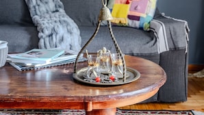 Un salon avec un canapé gris, un coussin matelassé aux couleurs vives, une table basse en bois ornée d’un élément décoratif en métal, et un tapis.