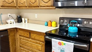 A kitchen with wooden cabinets, a stainless steel microwave, a black stove, and a teal kettle.
