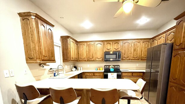 A kitchen with wooden cabinets, a stainless steel refrigerator, a microwave, a stove, and a ceiling fan.