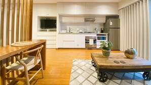 A modern kitchen with white cabinets, a built-in oven, and a refrigerator. There is a dining table with chairs and a small cart with a plant. - Elegante Loft en Barranco (Lima)