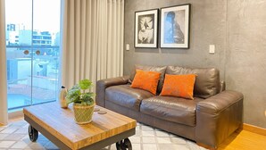 A living room with a brown leather sofa, two orange cushions, a wooden coffee table with a plant, and two framed pictures on the wall. - Elegante Loft en Barranco (Lima)