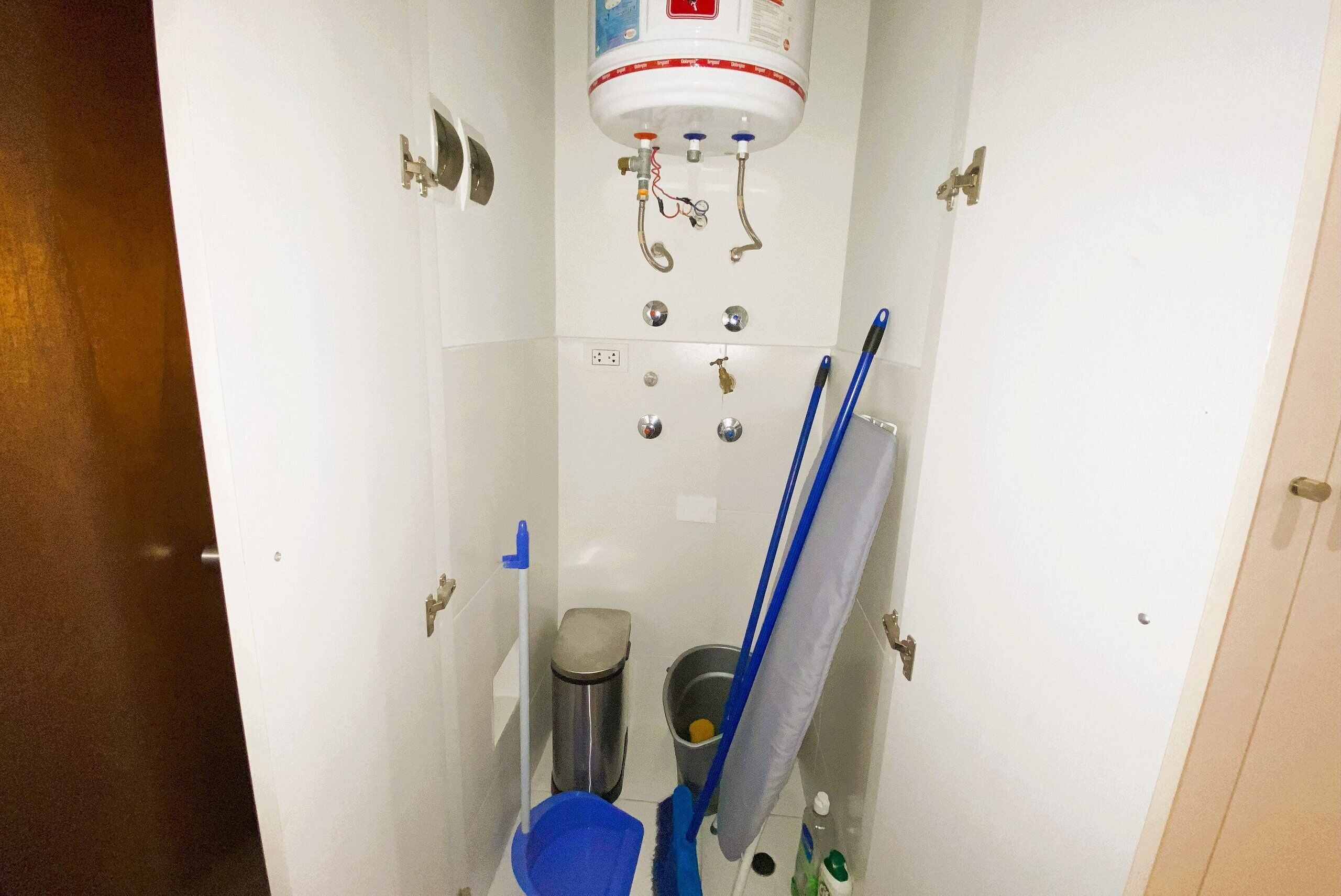 A bathroom with a water heater, a trash bin, a mop, and cleaning supplies.