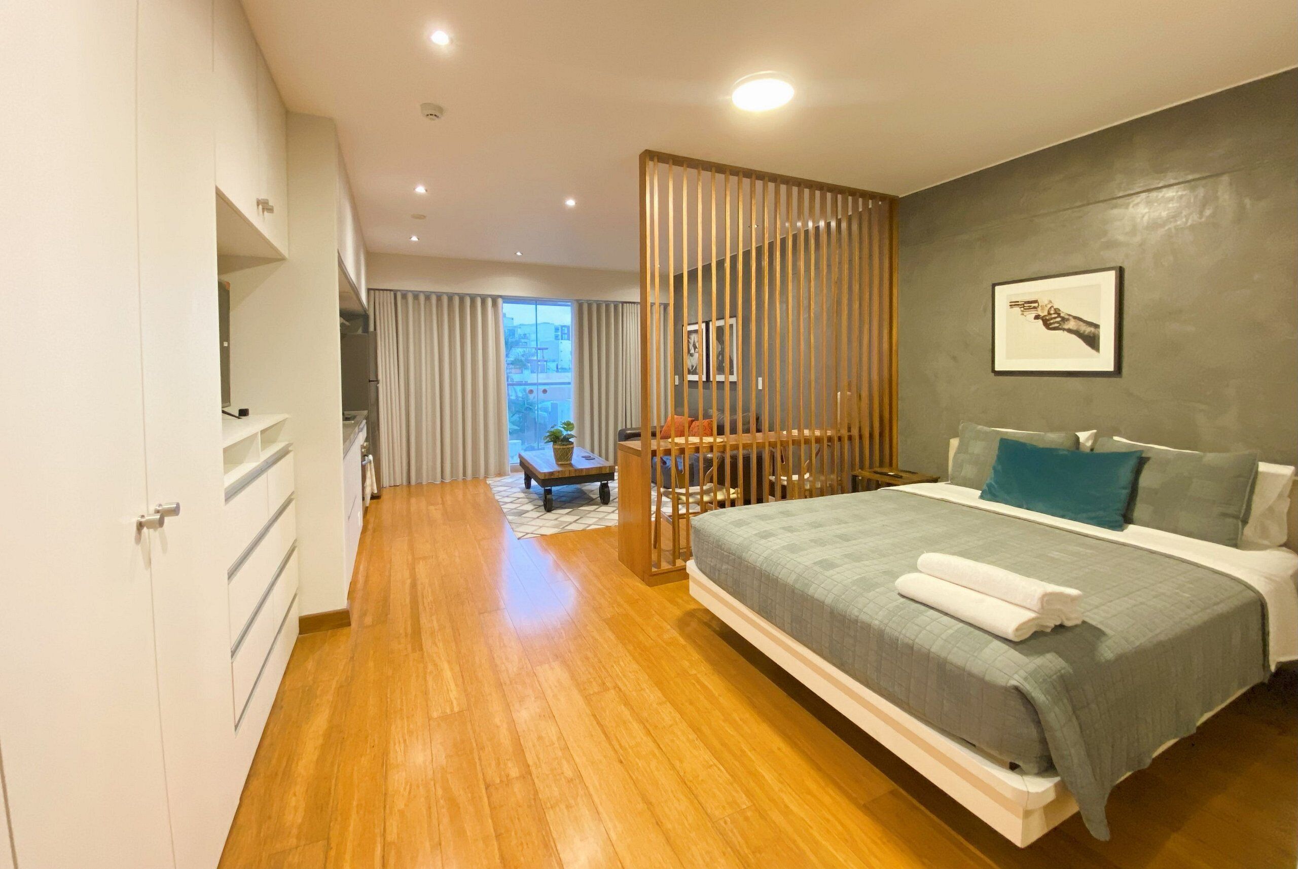 Ein modernes Schlafzimmer mit einem großen Bett, Holzboden und Blick auf die Stadt durch ein großes Fenster.