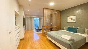 A modern bedroom with a large bed, wooden floor, and a view of the city through a large window. - Elegante Loft en Barranco (Lima)