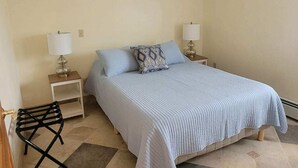 Una camera da letto con un letto, due comodini con lampade, una sedia nera e un cuscino decorato.