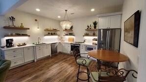 A modern kitchen with white cabinets, a stainless steel refrigerator, and a dining area with a wooden table and chairs. - Charming 2bedroom villa in the terrace level of the host home,Completely private (Hoschton)