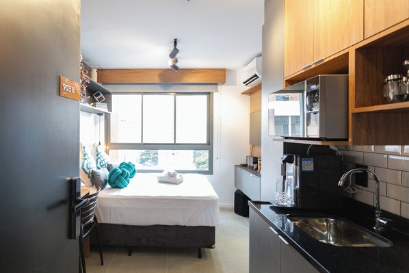 A compact bedroom with a bed, a window, and a kitchenette. - Go Balkon (Sao Paulo)