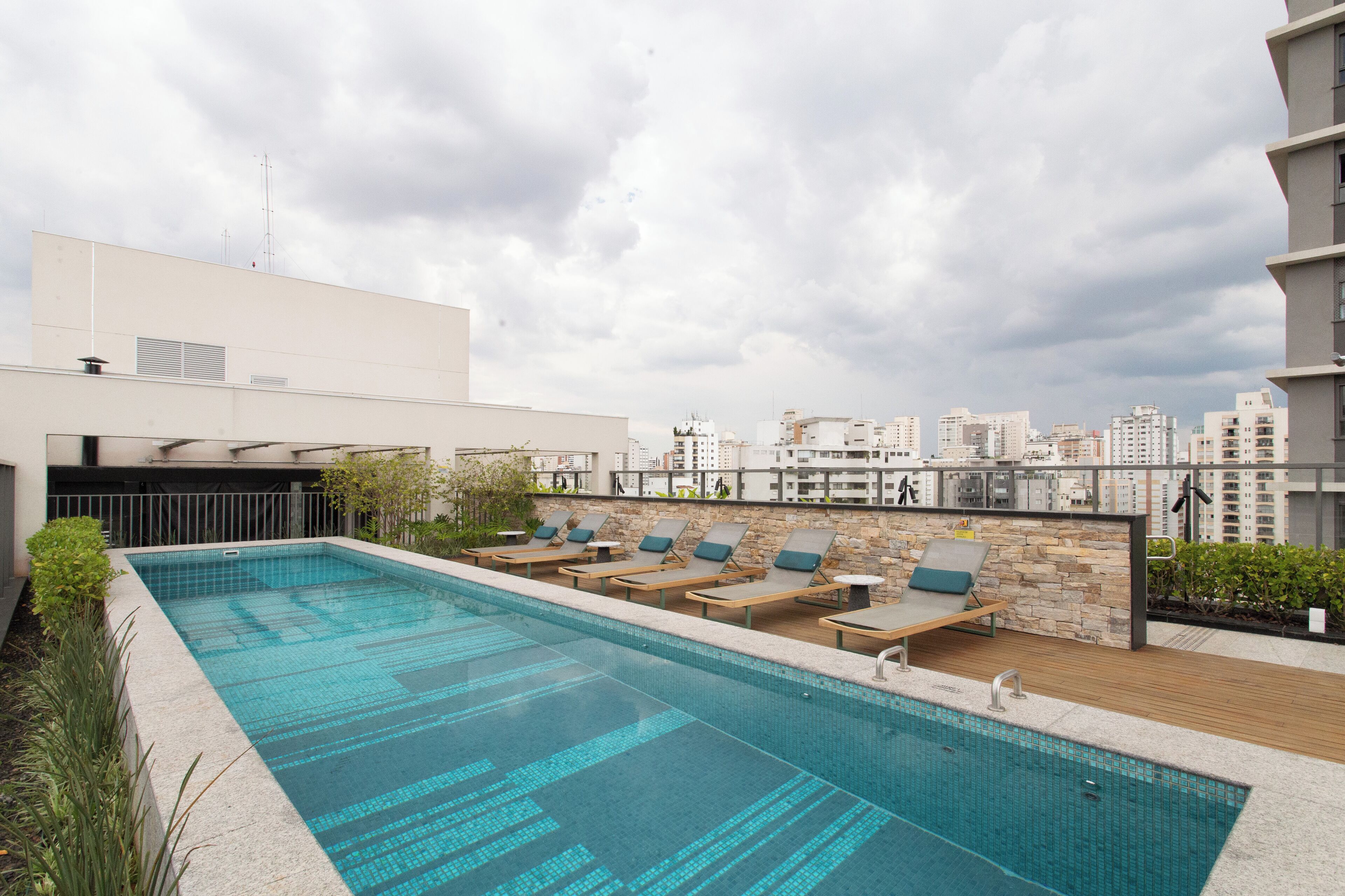 A rooftop swimming pool with lounge chairs and a cityscape view.