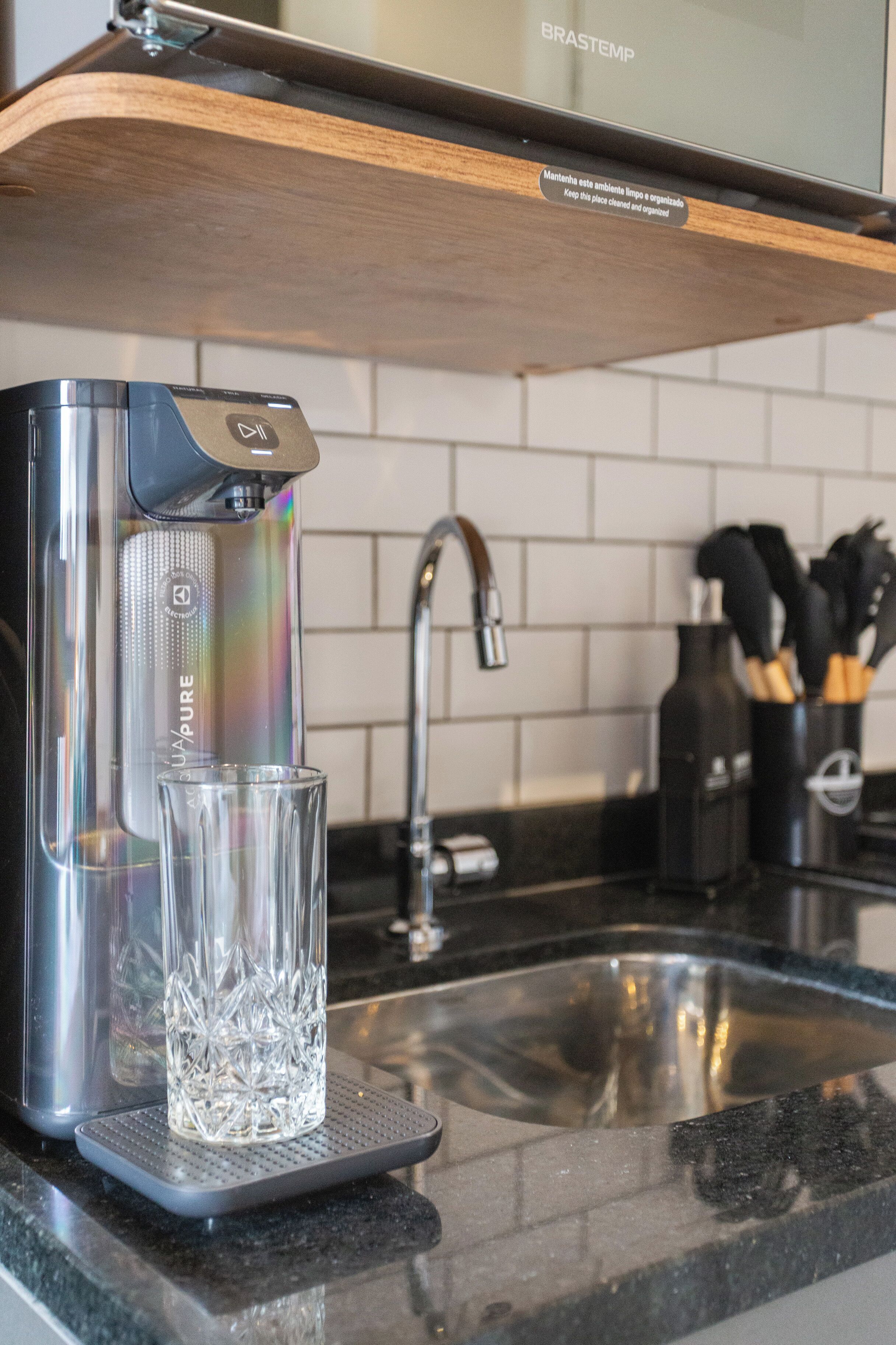 A kitchen with a water dispenser, a glass, and a sink.