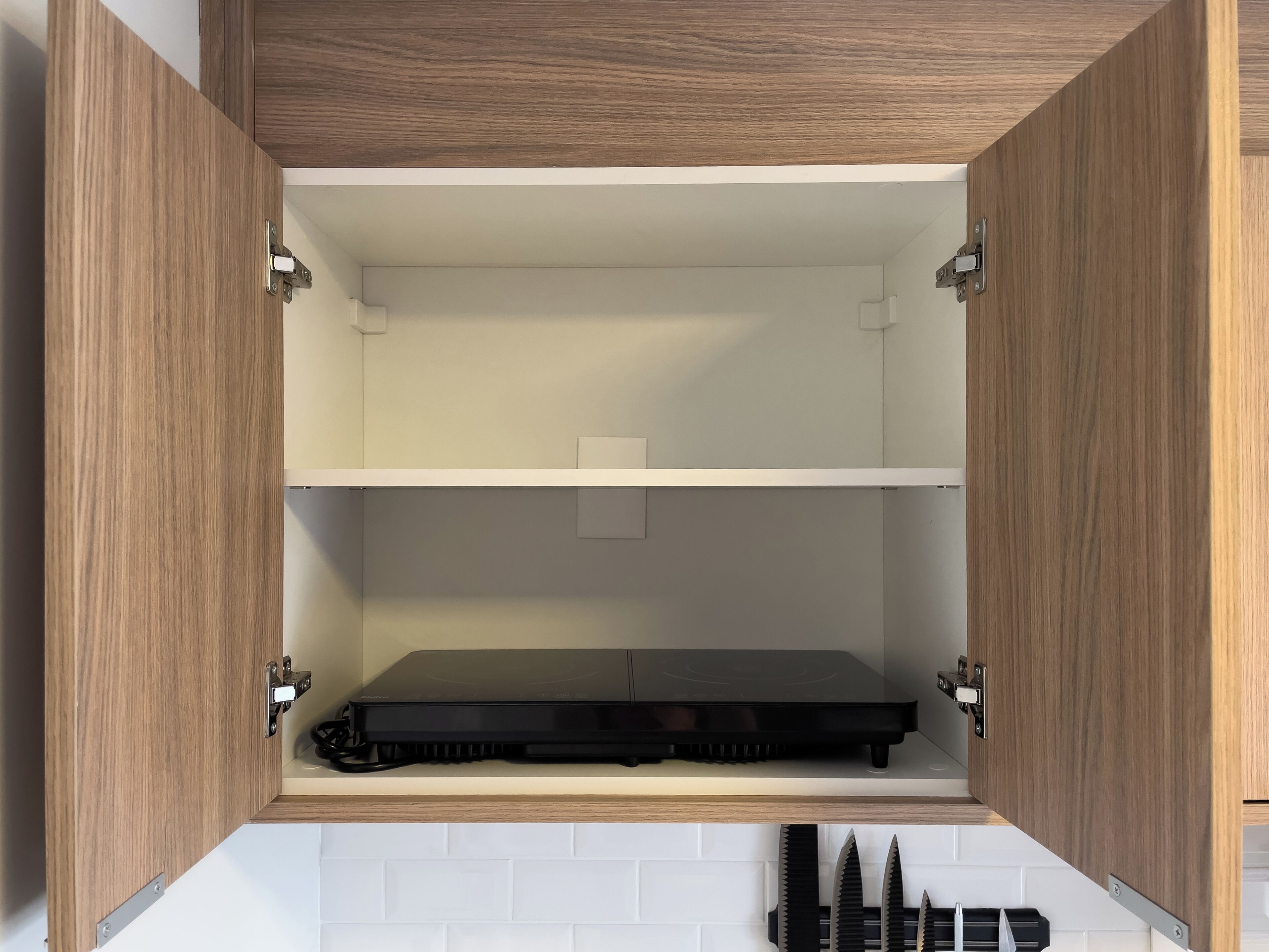 Ein Küchenschrank mit zwei Einlegeböcken, einem schwarzen Gerät auf der unteren Ablage und einem Messerblock an der unteren Schranktür.