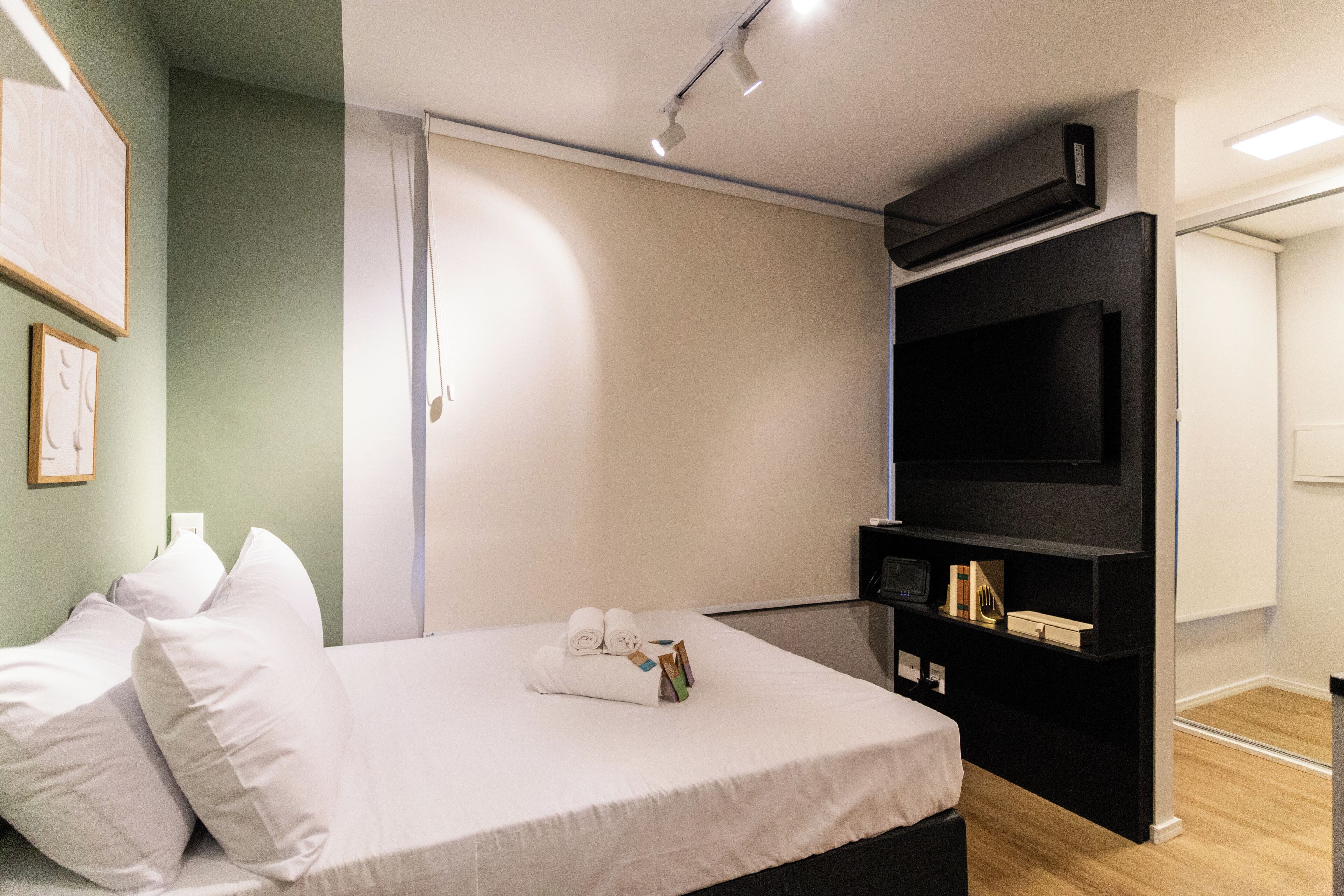 A modern hotel room with a bed, white linens, a flat-screen TV, and a black entertainment unit.