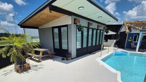 Een modern huis met een zwembad, met een overdekt terras en zitplaatsen, beplant met potten.