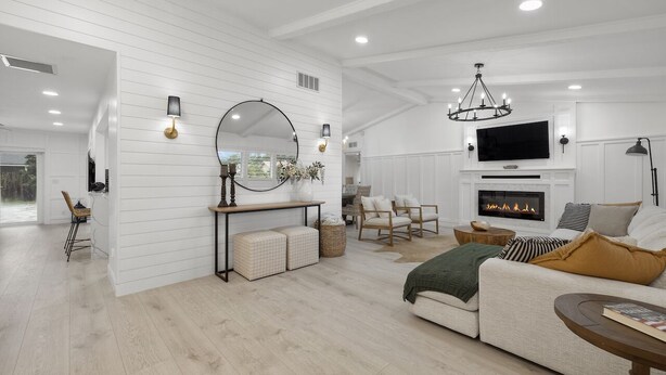 A modern living room with a fireplace, white paneled walls, and a large flat-screen TV. - Luxury Wellington Pool Home! (Wellington)