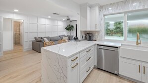 A modern kitchen with white cabinetry, a marble island, and a built-in dishwasher. - Luxury Wellington Pool Home! (Wellington)