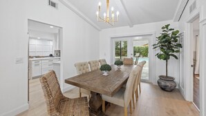 A dining room with a wooden table, beige chairs, and a chandelier. There is a potted plant and a wicker chair. - Luxury Wellington Pool Home! (Wellington)