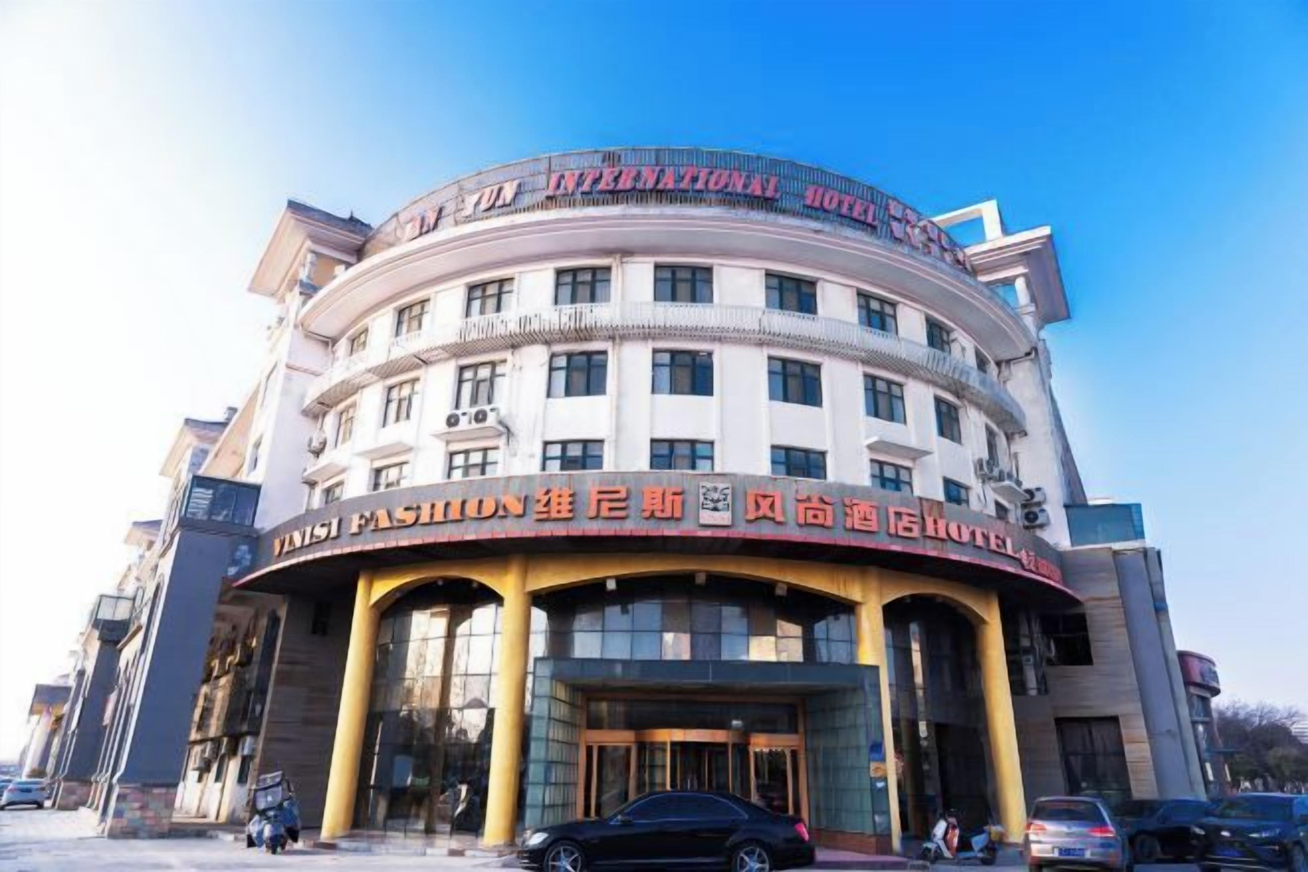 Un immeuble à plusieurs étages doté d’une façade incurvée, avec une enseigne « International Hotel » au sommet et une enseigne « FANSI Fashion Building » en bas.