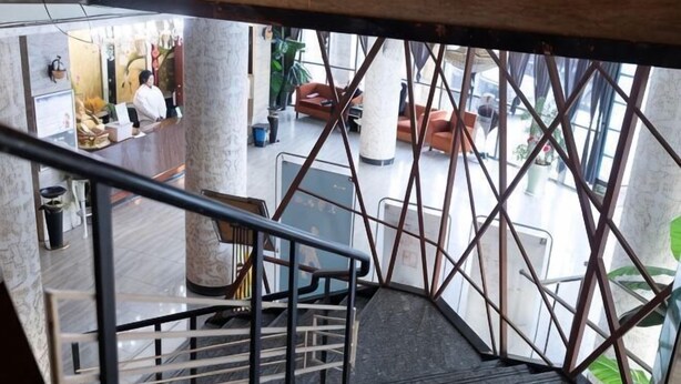A staircase with a metal railing leading to a lobby area with seating and a reception desk.
