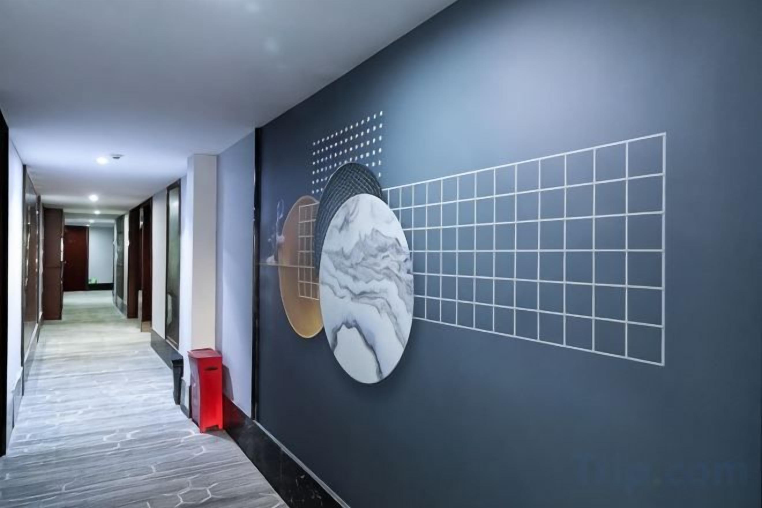 A hallway with a patterned floor, a wall-mounted artwork, and a trash bin.