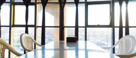 A conference room with a glass table and two chairs, large windows with curtains, and a view of the city.