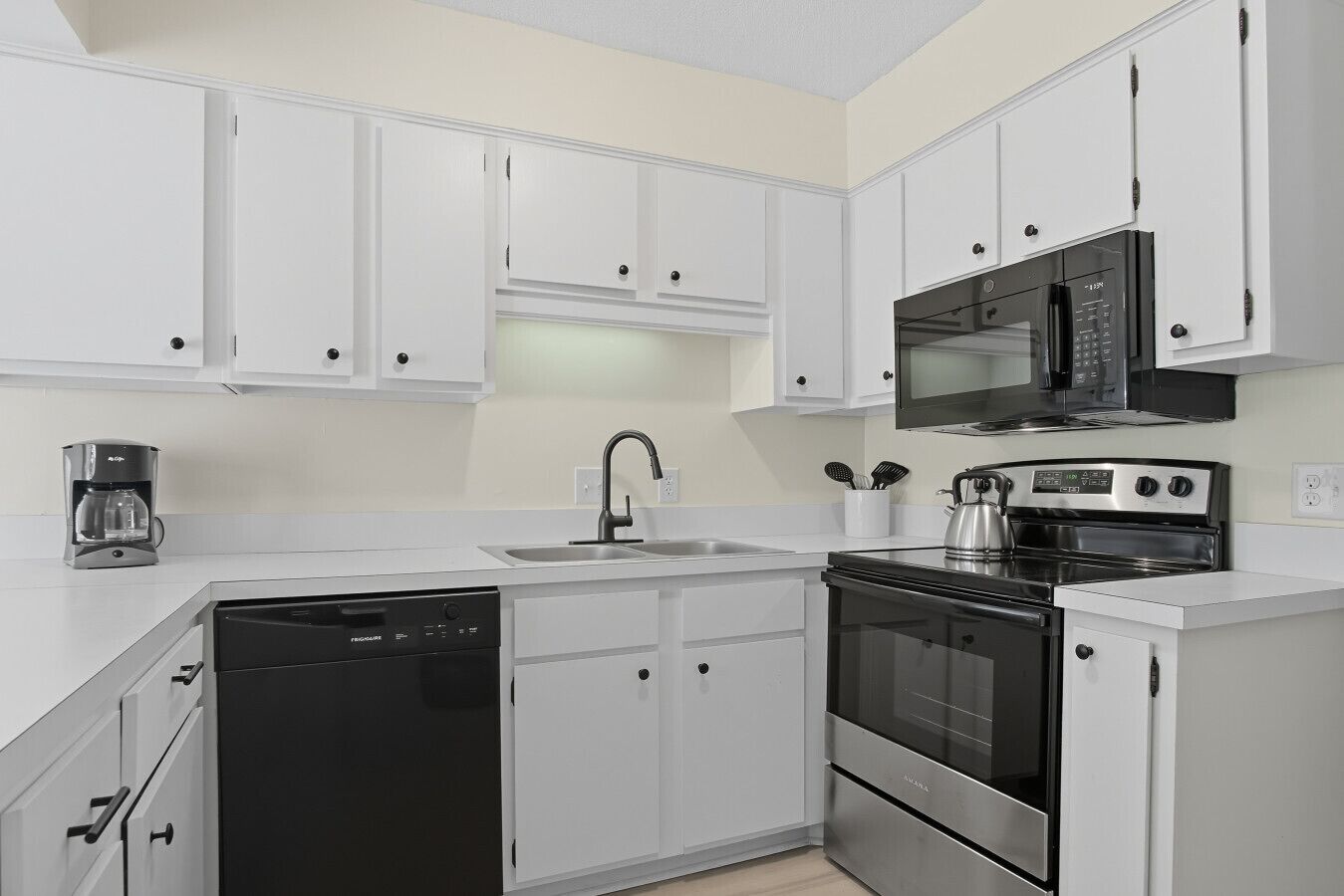 Una cocina moderna con armarios blancos, lavavajillas, estufa y microondas.