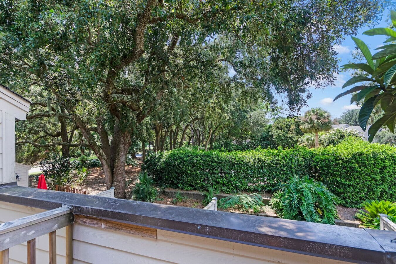 A balcony with a view of a garden featuring various trees and well-maintained hedges.