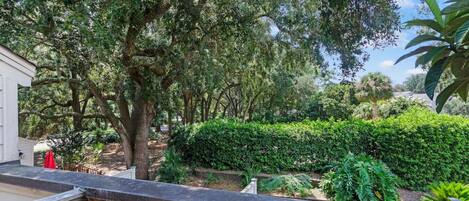 A balcony with a view of a garden featuring various trees and well-maintained hedges.