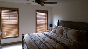 A bedroom with a bed, two windows with blinds, a ceiling fan, and a bedside lamp. - Spacious 5-bedroom townhome with WiFi and AC in charming Bolton Landing (Bolton Landing)