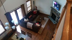 A living room with a sofa, coffee table, fireplace, TV, and dining area. - Spacious 5-bedroom townhome with WiFi and AC in charming Bolton Landing (Bolton Landing)
