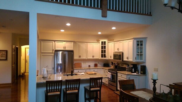 A spacious kitchen with white cabinets, a stainless steel refrigerator, a microwave, and a stove. There are two wooden chairs at the island and a dining table with a candle. - Spacious 5-bedroom townhome with WiFi and AC in charming Bolton Landing (Bolton Landing)