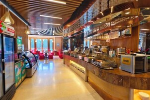 A modern hotel lobby with a curved reception desk, vending machines, and a seating area with red chairs.
