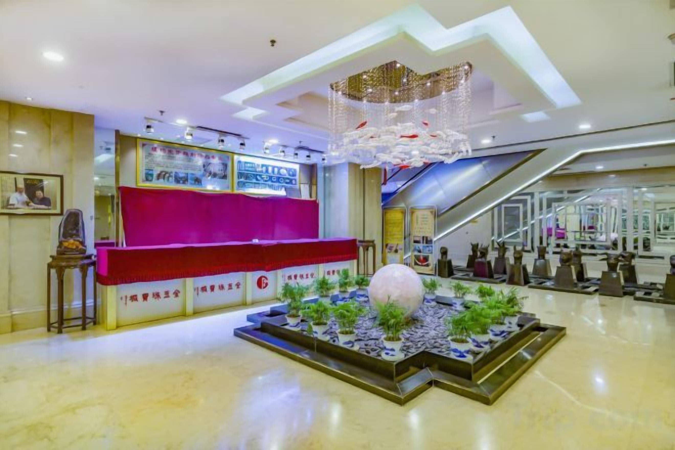 A reception area with a red counter, a decorative chandelier, and a small indoor garden.