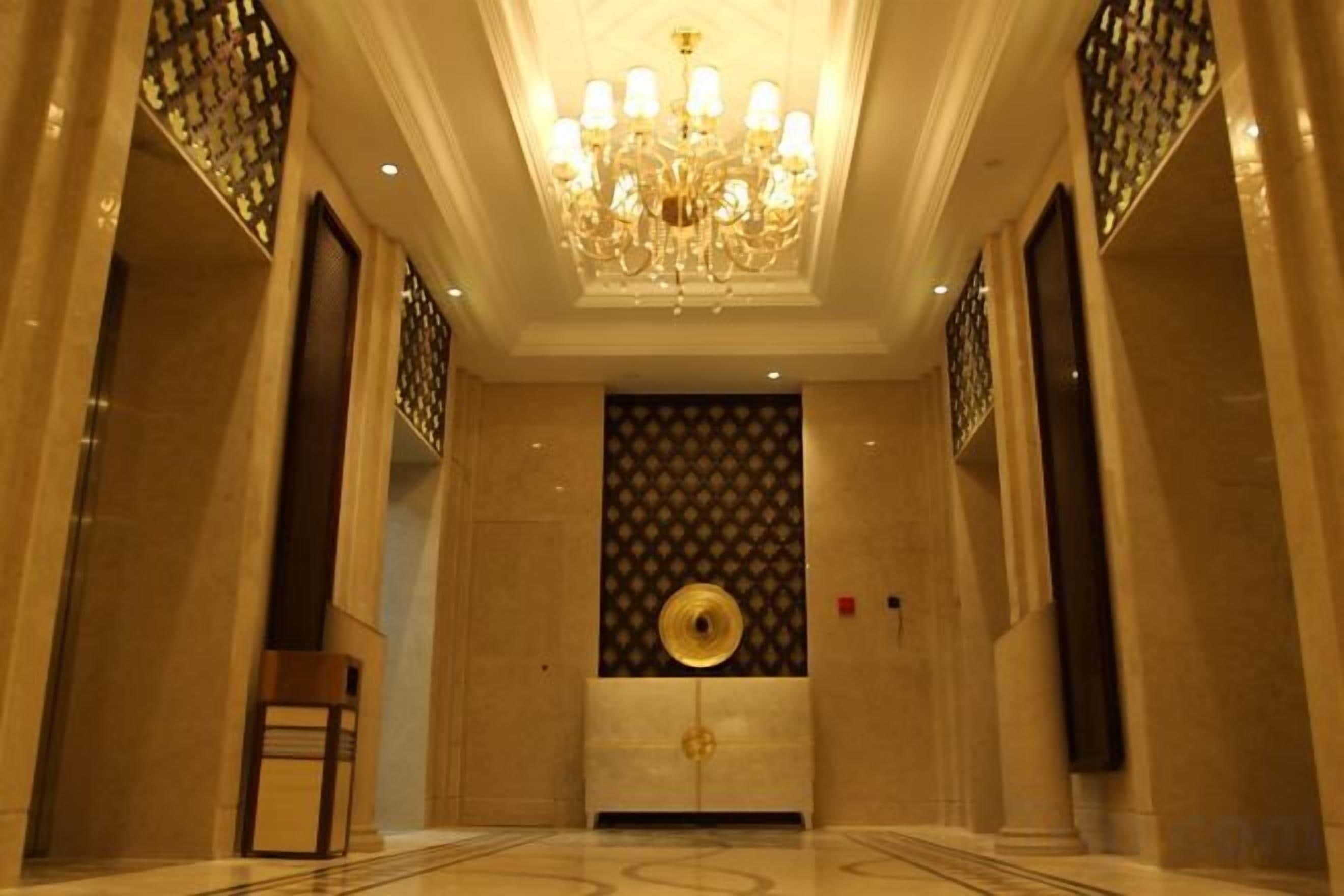 A hallway with a chandelier, patterned wall, and a door with a circular design.