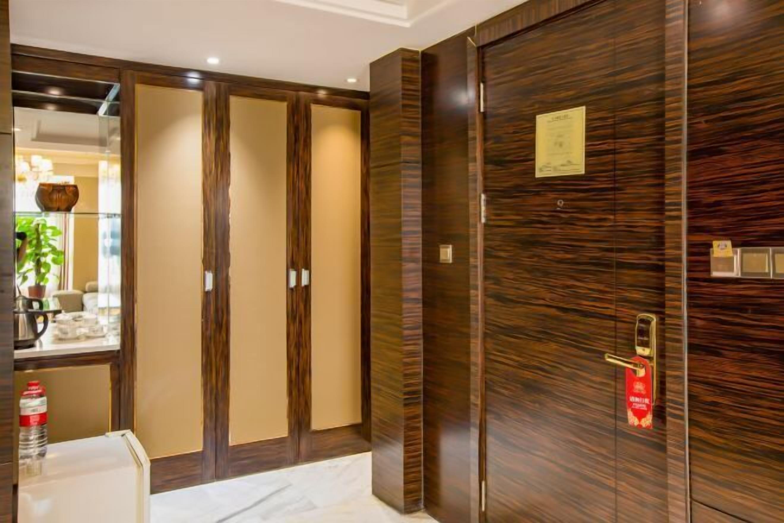 A hotel room with a large wooden wardrobe, a mirror, and a small table with a bottle.