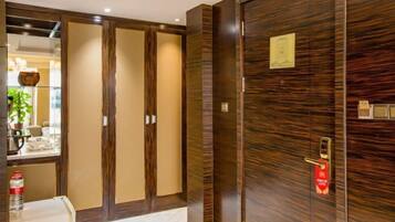 A hotel room with a large wooden wardrobe, a mirror, and a small table with a bottle.