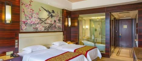 A hotel room with two beds, a large floral artwork on the wall, a bathroom with a glass shower, and a wooden floor.