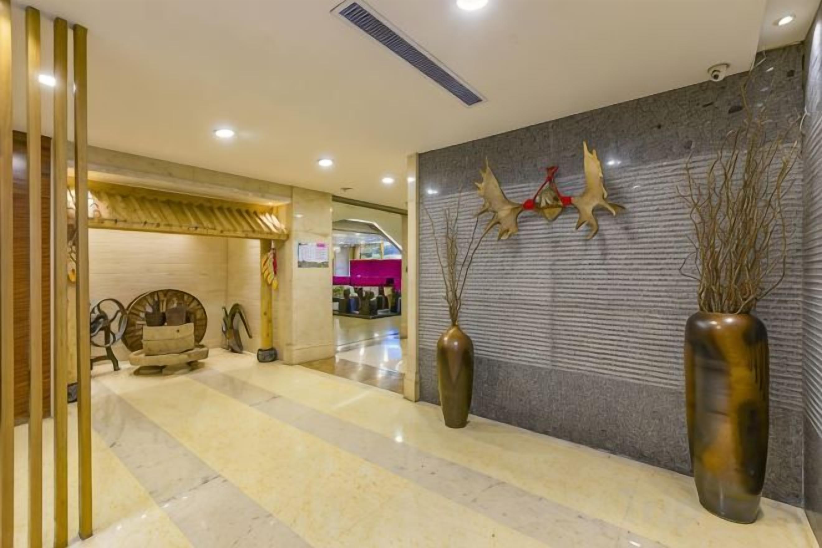 A hotel lobby with a reception desk, a seating area, and a decorative wall with a vase and branches.