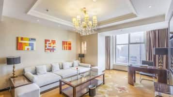 A modern living room with a sofa, coffee table, and decorative lamps. There are large windows with curtains, a chandelier, and artwork on the walls.
