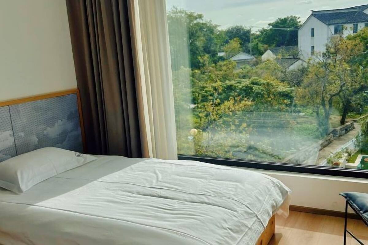 Une chambre avec une grande fenêtre, un lit et une vue sur un quartier résidentiel.