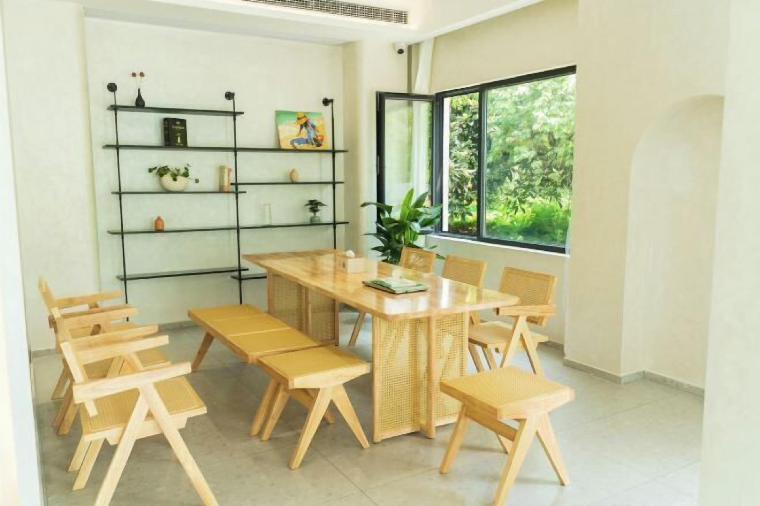 Zona de menjador amb taula i cadires de fusta, una prestatgeria i una finestra que dona a vistes de vegetació.