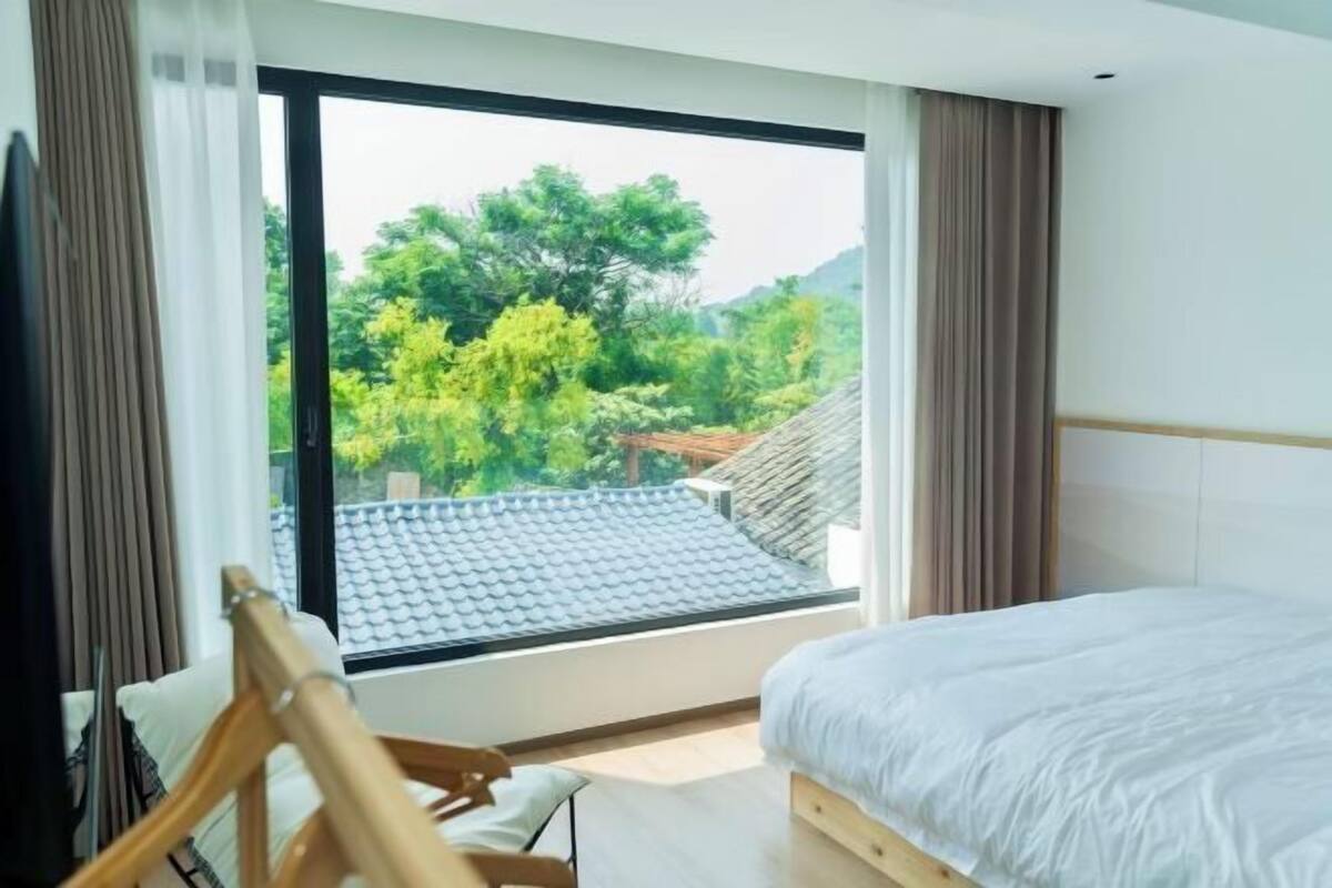 Une chambre avec une grande fenêtre, un lit et une chaise en bois.