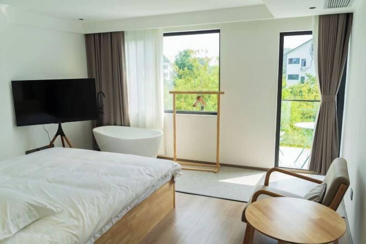 Une chambre d’hôtel avec un lit, une télévision, une baignoire, un balcon avec une balançoire en bois et une petite table.