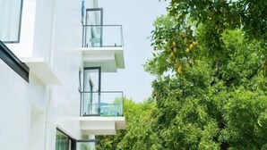 Un edificio moderno con varios balcones y un árbol frondoso en el fondo.