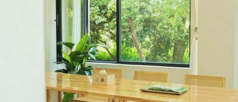 Comedor con mesa y sillas de madera, una planta en maceta y ventana con vista a árboles.
