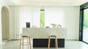 Una cocina moderna con encimera de mármol, dos taburetes y una ventana con cortinas.