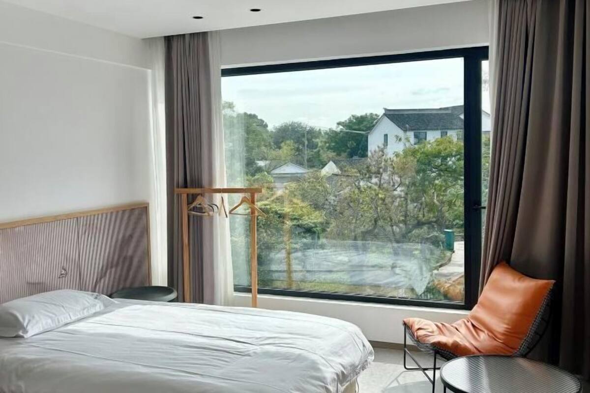 Une chambre d’hôtel moderne avec une grande fenêtre, un lit, une chaise et une petite table.