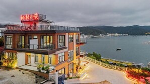 Un hôtel moderne doté d’une façade en verre, d’une terrasse sur le toit et offrant une vue sur une étendue d’eau.