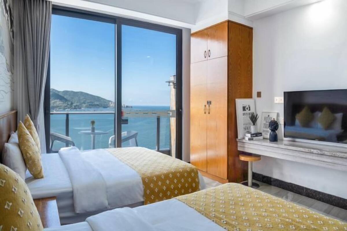 Een hotelkamer met twee bedden, een televisie, een minibar en uitzicht op zee.