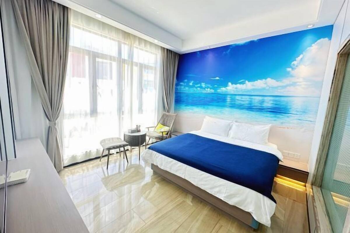 Een hotelkamer met een bed, een tafeltje, een stoel en een groot raam met gordijnen.